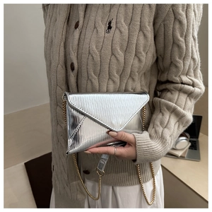 Detail of silver pleated envelope bag with gold chain strap on knit sweater