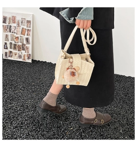 Detail of cream woven bucket bag with long strap and cute plush brown animal charm