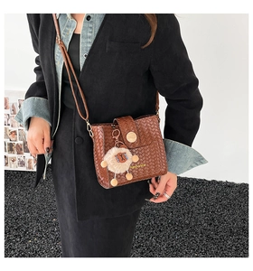Brown woven crossbody bag with round wooden buckle and lion plush pendant detail