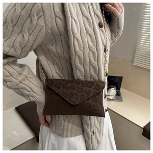 Brown leopard print envelope crossbody bag with gold chain strap on beige cardigan