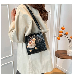 Detail of black woven crossbody bag with cute teddy bear charm and gold brand lettering