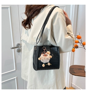 Detail of black woven bucket bag featuring V-shaped texture and plush bear charm
