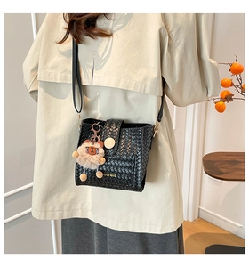 Detail of black woven crossbody bag with gold buckle and plush animal keychain