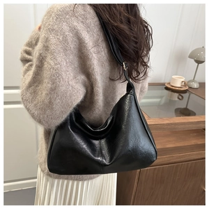 Detail of black vintage shoulder bag with textured leather and adjustable strap on a model