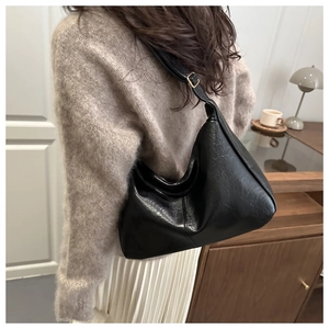 Side view of a black faux leather hobo bag worn by a model in a cozy indoor setting