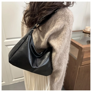 Detail view of the black matte leather hobo bag shoulder strap and gold hardware attachment