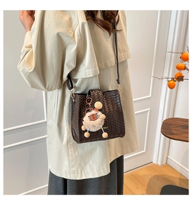 Detail of dark brown woven bucket bag with plush charm on a crossbody shoulder strap