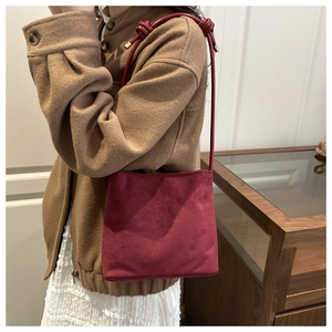 Close-up of red suede shoulder bag with fashion and classic embossed text and knotted strap