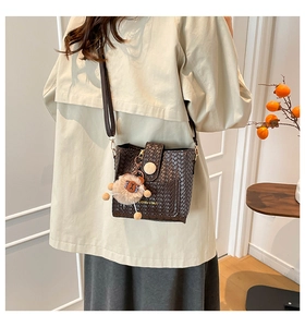 Close-up of dark brown woven bucket bag with wood buckle and cute lion plush charm