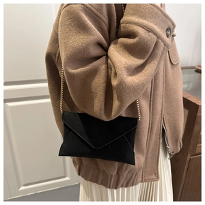Detail of minimalist black suede envelope bag with elegant gold chain strap on model