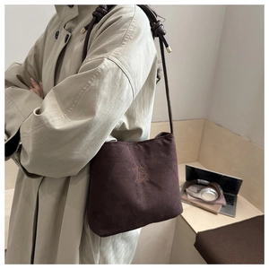 Detail of dark brown suede shoulder bag with embroidered text and cord strap on model