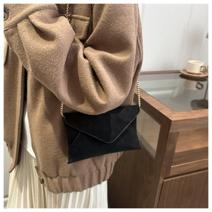Detailed view of a black envelope crossbody bag with gold chain on a styled model