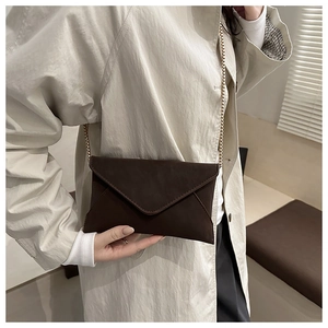 Detail of dark brown envelope crossbody bag with gold chain and soft leather texture