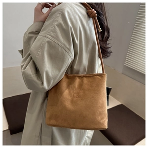 Close-up of brown suede bucket bag with fashion and classic embossed text and knotted strap