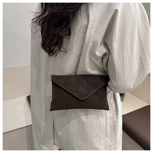 Brown envelope crossbody bag with gold chain strap shown on a model's shoulder