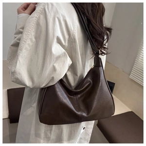 Detailansicht einer dunkelbraunen Hobo-Tasche aus mattem Leder, getragen zum Trenchcoat