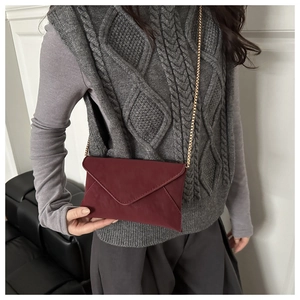 Detail of burgundy envelope crossbody bag with gold chain strap on model shoulder
