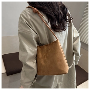 Close-up of caramel brown suede bucket bag with knotted shoulder strap and embossed text
