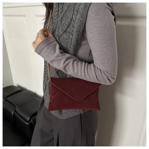 Close-up of elegant burgundy envelope crossbody bag with a fine gold chain strap
