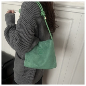 Detail of mint green suede bucket bag with knotted shoulder strap and embossed lettering