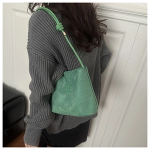 Side view of a green suede bucket bag with round rope strap on a model's shoulder