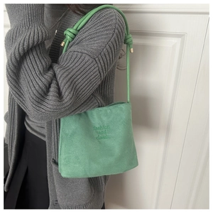 Detail of light green bucket bag showing knot decoration and embossed fashion text