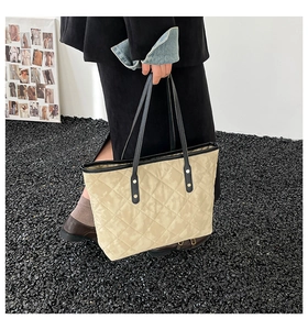 Close-up of quilted beige tote bag showing black faux leather handles and gold rivet details