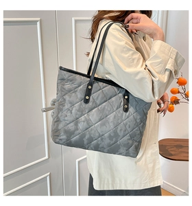 Detail of grey quilted tote bag featuring camouflage pattern and black leather handles