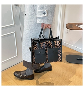 Detail view of a large leopard print tote bag with black handles and front pockets
