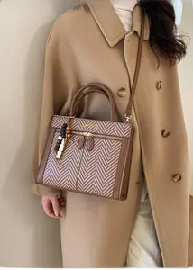 Detail of a brown leather and plaid fabric crossbody bag with a wooden bead charm