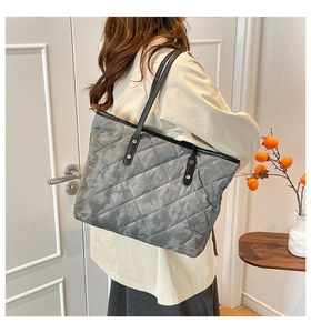 Detailed side view of large grey quilted tote bag with black straps and gold rivets