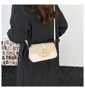 Cream saddle bag with woven flap detail and gold metal clasp shown on a black coat