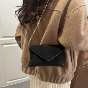 Minimalist black suede envelope crossbody bag with gold chain strap on model