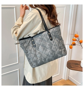 Detail of grey quilted tote bag with black leather straps and gold metal rivets