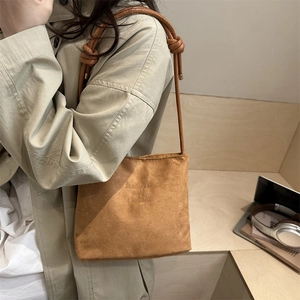 Suede bucket bag in tan with embossed text and decorative knotted strap on a model