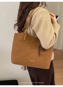 Detail of a brown tote bag featuring golden lettering and a woven decorative pendant