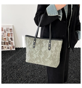 Détail d'un sac cabas matelassé avec anses en cuir noir et anneaux dorés sur le mannequin