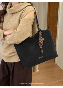 Close-up of black suede tote bag with contrast stitching and metal abacus charm detail