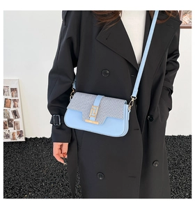 Detail of light blue saddle bag featuring tweed textured flap and gold geometric clasp