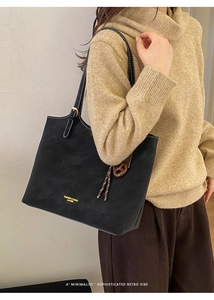 Detail of black leather tote bag with white contrast stitching and pretzel charm