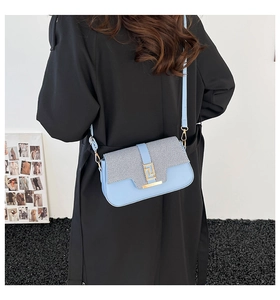 Close-up of light blue crossbody bag with striped flap and gold buckle on black coat