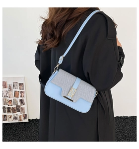 Detail of light blue crossbody bag with textured silver flap and golden buckle on a model