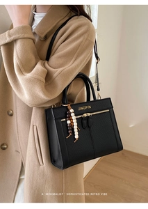 Detail of black matte tote bag with gold zipper and wooden bead charm on shoulder