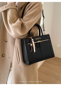 Detail of black pebbled leather crossbody bag with gold logo and beaded accessory