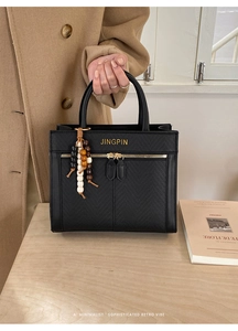 Detail of black textured square handbag with gold logo and colorful beaded charm