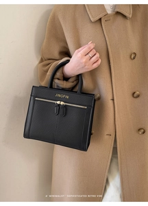 Detail of minimalist black textured leather handbag with gold logo and dual zipper design