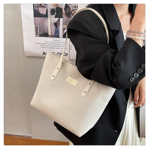 Detail of beige corduroy tote bag with gold rivets and logo shown on model shoulder