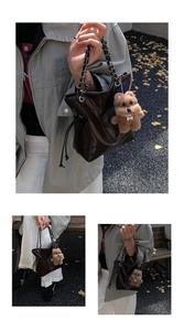 Détail du sac seau en cuir foncé avec bandoulière chaîne, cordon et pendentif ourson