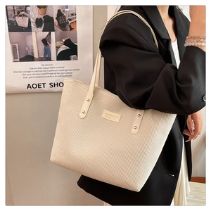 Detail view of large beige corduroy tote bag worn with a black blazer for urban style
