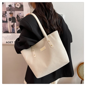 Detailed close-up of cream corduroy tote bag texture with minimalist branding and rivet detail